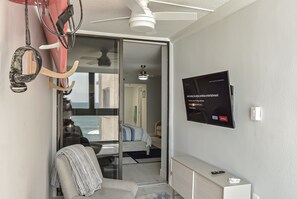 A modern hotel room with a bed, a TV mounted on the wall, a ceiling fan, and a view of the sea through a sliding door. - Beautiful home away from home with direct ocean views. (New Smyrna Beach)