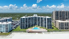 A multi-story hotel with a central courtyard pool, surrounded by lush greenery and a clear blue sky.