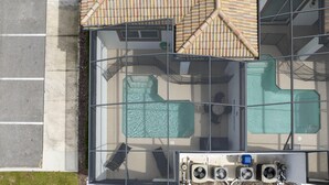 Ein Luftbild eines Hotels mit einem von Glas umschlossenen Poolbereich, einer überdachten Sitzgelegenheit im Freien und mehreren Klimaanlagen.