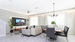 Ein modernes Wohnzimmer mit einer Couch, einem Esstisch, Stühlen und einem an der Wand befestigten Fernseher.