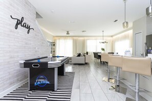 A modern living room with a foosball table, a sofa, and a dining area with bar stools.