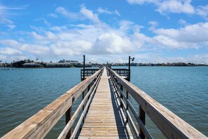 A wooden pier extending into calm water with a clear sky and distant buildings. - Little Bay Club by Miss Kitty’s (Rockport)