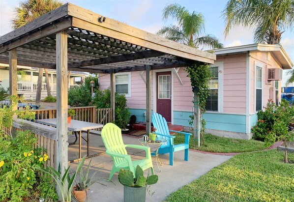 A covered patio area with a wooden pergola, two chairs, a table, and potted plants.