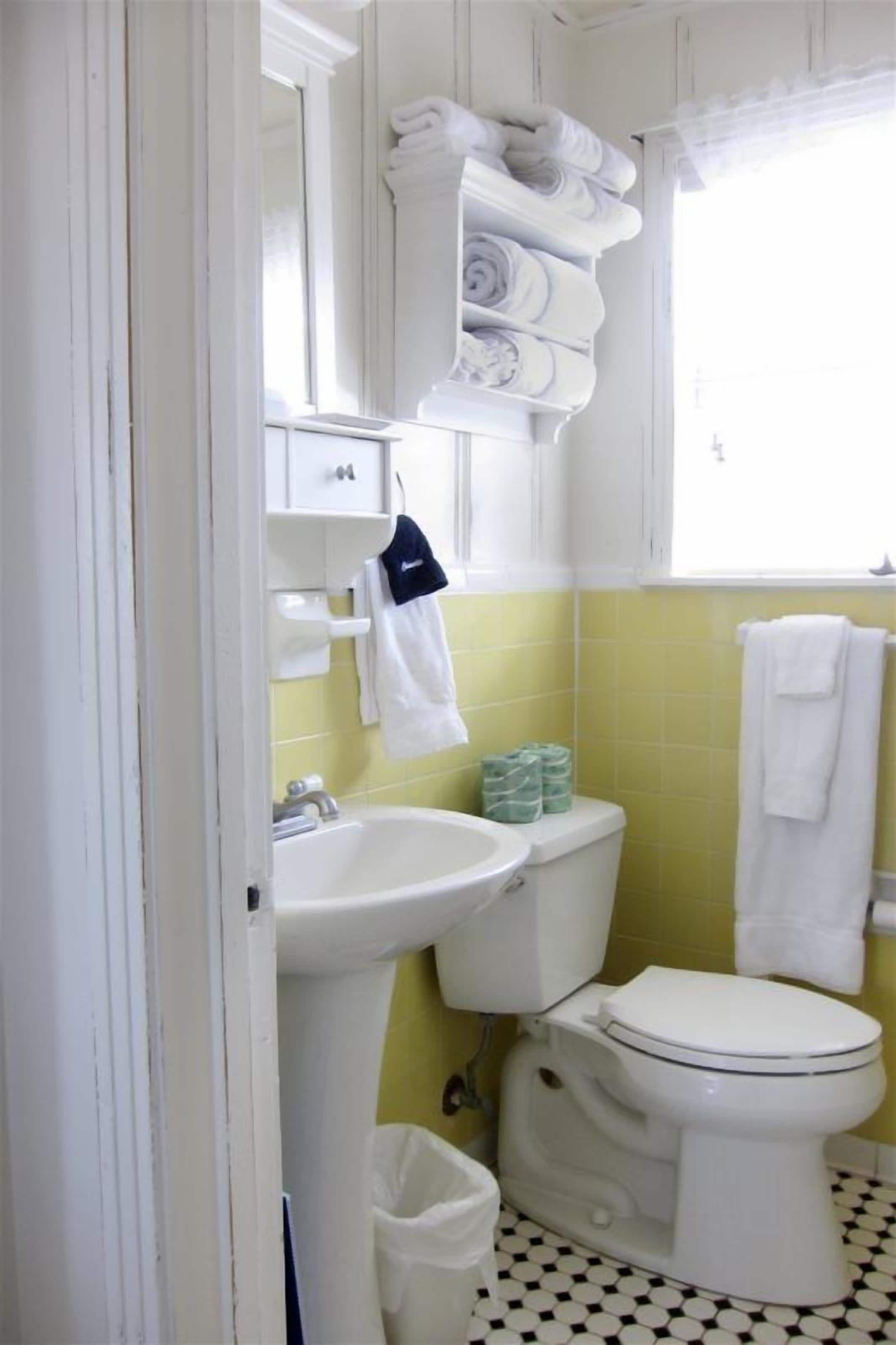 Une salle de bain avec un lavabo blanc, des toilettes et un porte-serviettes sur lequel sont pliées des serviettes.