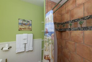 Ein Badezimmer mit grünen Wänden, einer Duschvorhang mit Strandmotiv und einem Schild mit der Aufschrift 'No Wake Zone!'