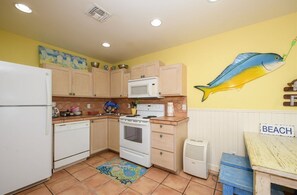 A kitchen with wooden cabinets, a white refrigerator, a microwave, an oven, and a small table with a 'BEACH' sign. - Little Bay Club by Miss Kitty’s (Rockport)