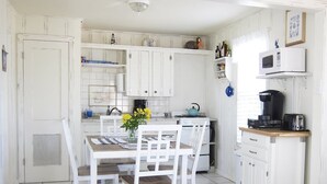 A compact kitchen with white cabinetry, a dining table with chairs, a stove, a microwave, and a coffee maker. - Little Bay Club by Miss Kitty’s (Rockport)