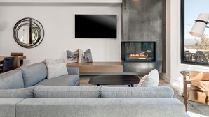 Una sala de estar moderna con un sofá gris, un televisor de pantalla plana, una chimenea y un ventanal grande.