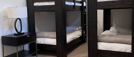 A room with three bunk beds, a small desk with a lamp, and a power outlet.