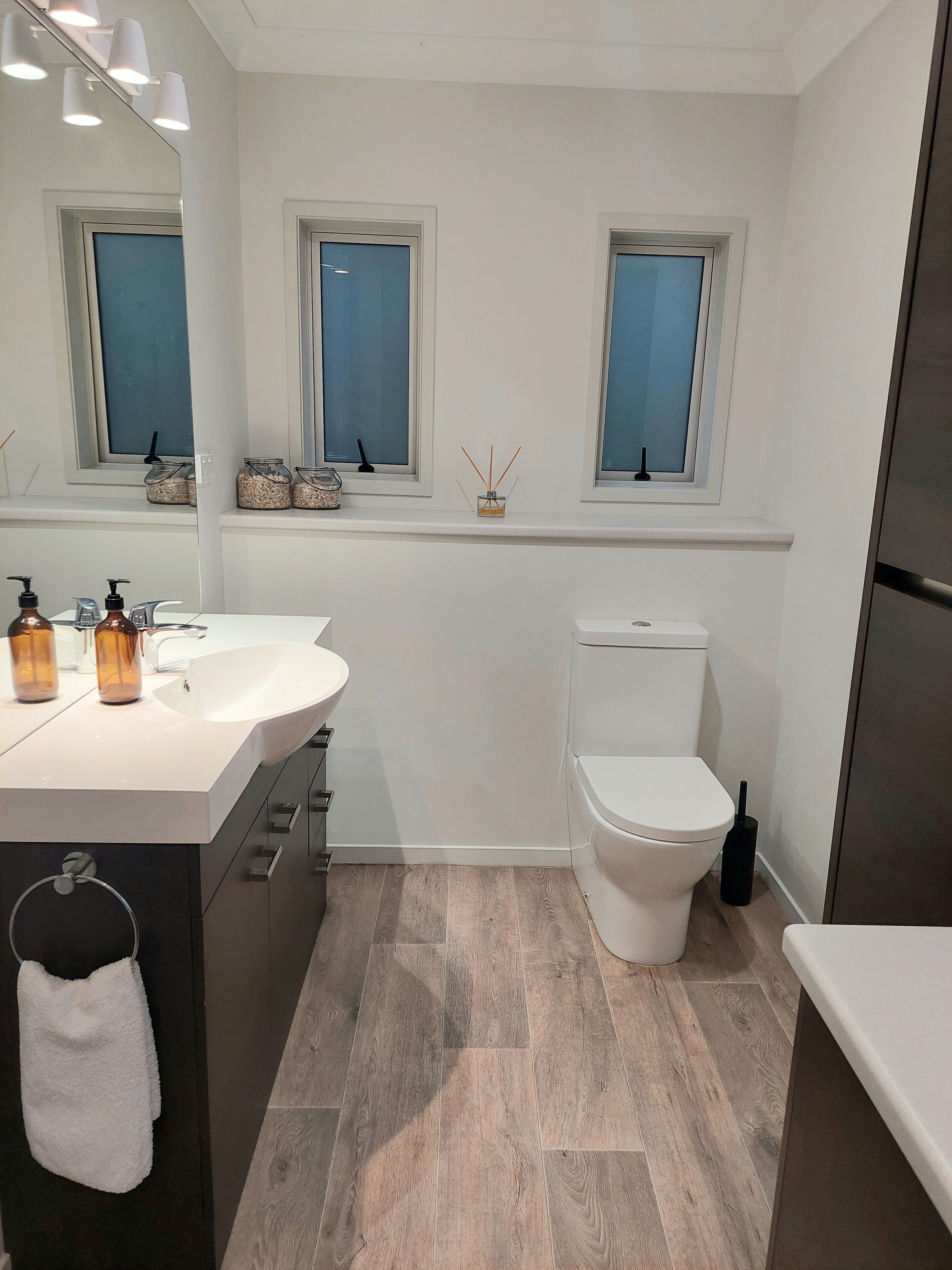 Une salle de bain moderne avec un lavabo blanc, deux fenêtres, des toilettes et un miroir.