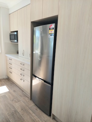 Une cuisine équipée d’un réfrigérateur en acier inoxydable, de meubles de rangement en bois, d’un four à micro-ondes et d’un plan de travail.