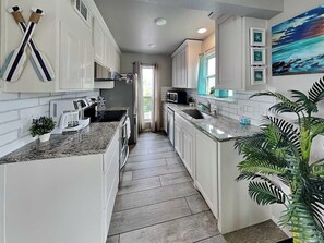 A kitchen with white cabinets, granite countertops, and a view to the outside. - Rockport Racquet and Yacht Club by Miss Kitty’s (Rockport)