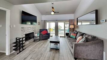 A spacious living room with a fireplace, a sofa, a coffee table, and a TV mounted on the wall.