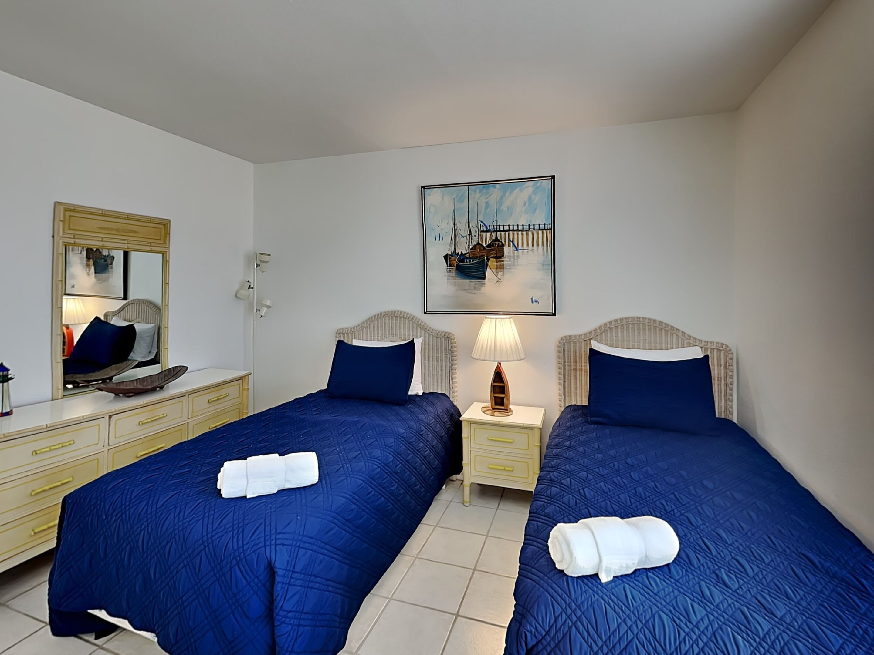 Ein Hotelzimmer mit zwei Betten, einem Spiegel, einem Gemälde, einer Lampe und einem Schminktisch.