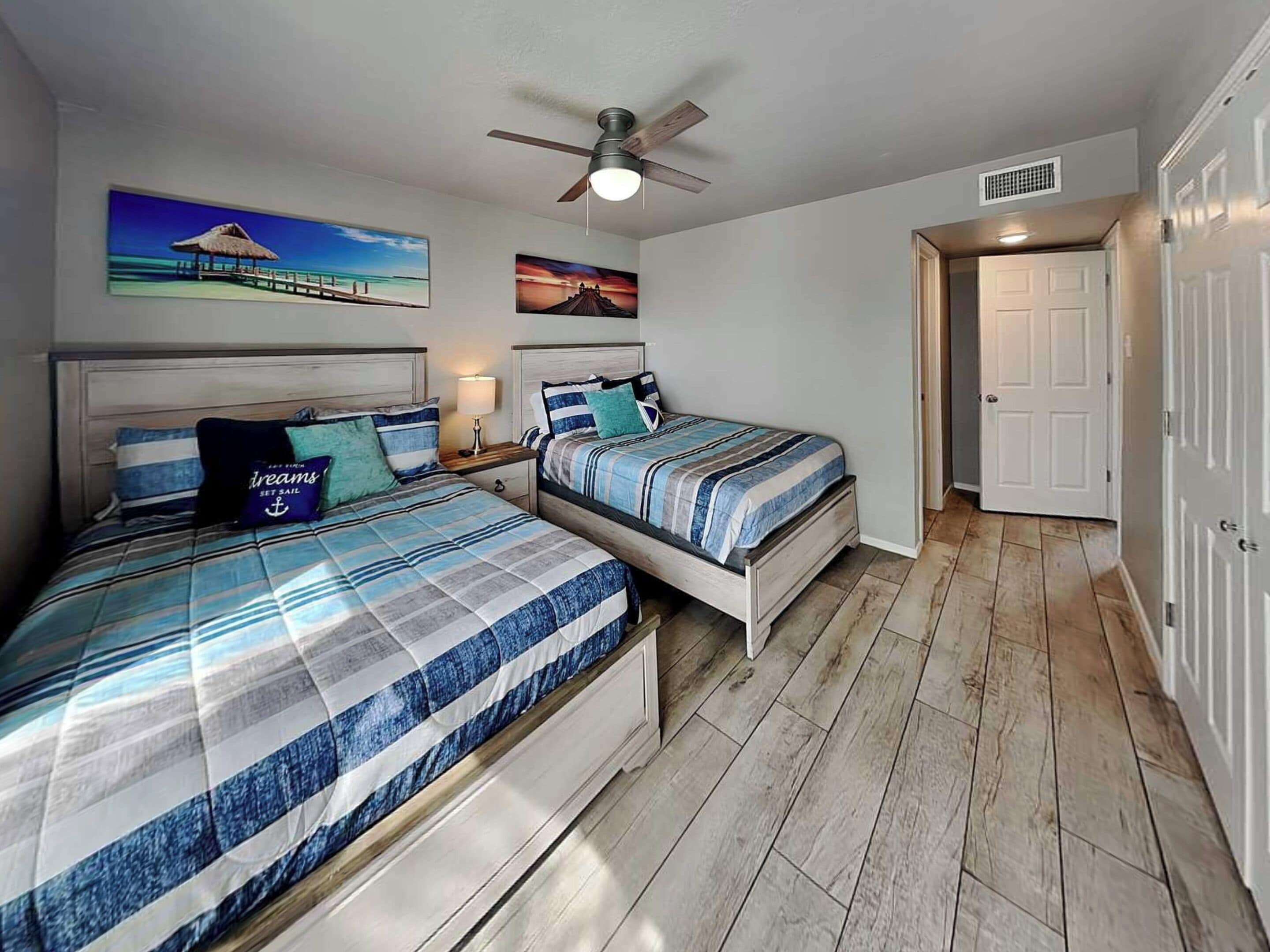 A bedroom with two beds, a ceiling fan, and artwork on the walls.