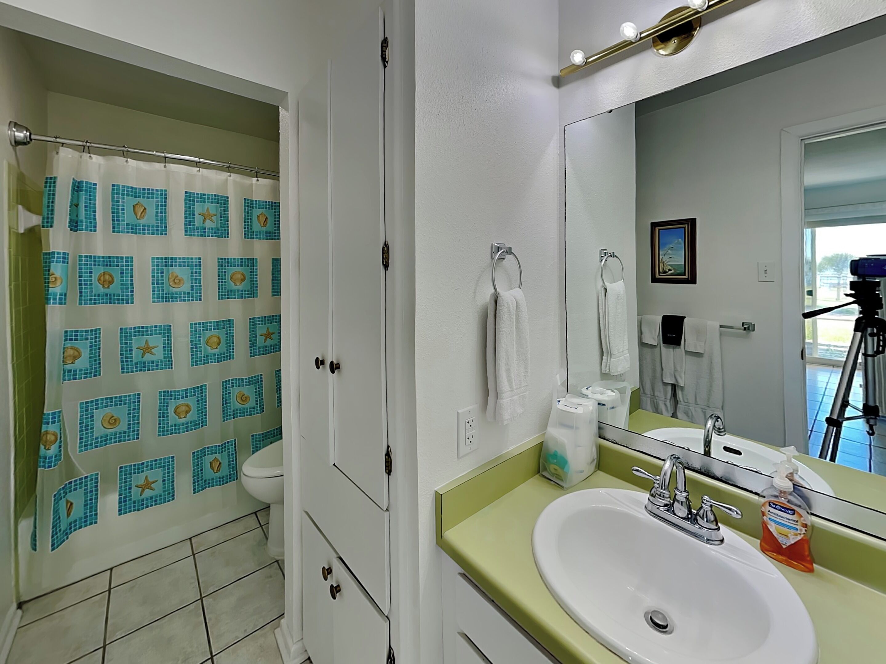 A bathroom with a shower curtain, a sink with a mirror, and a toilet.