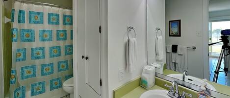 A bathroom with a shower curtain, a sink with a mirror, and a toilet.