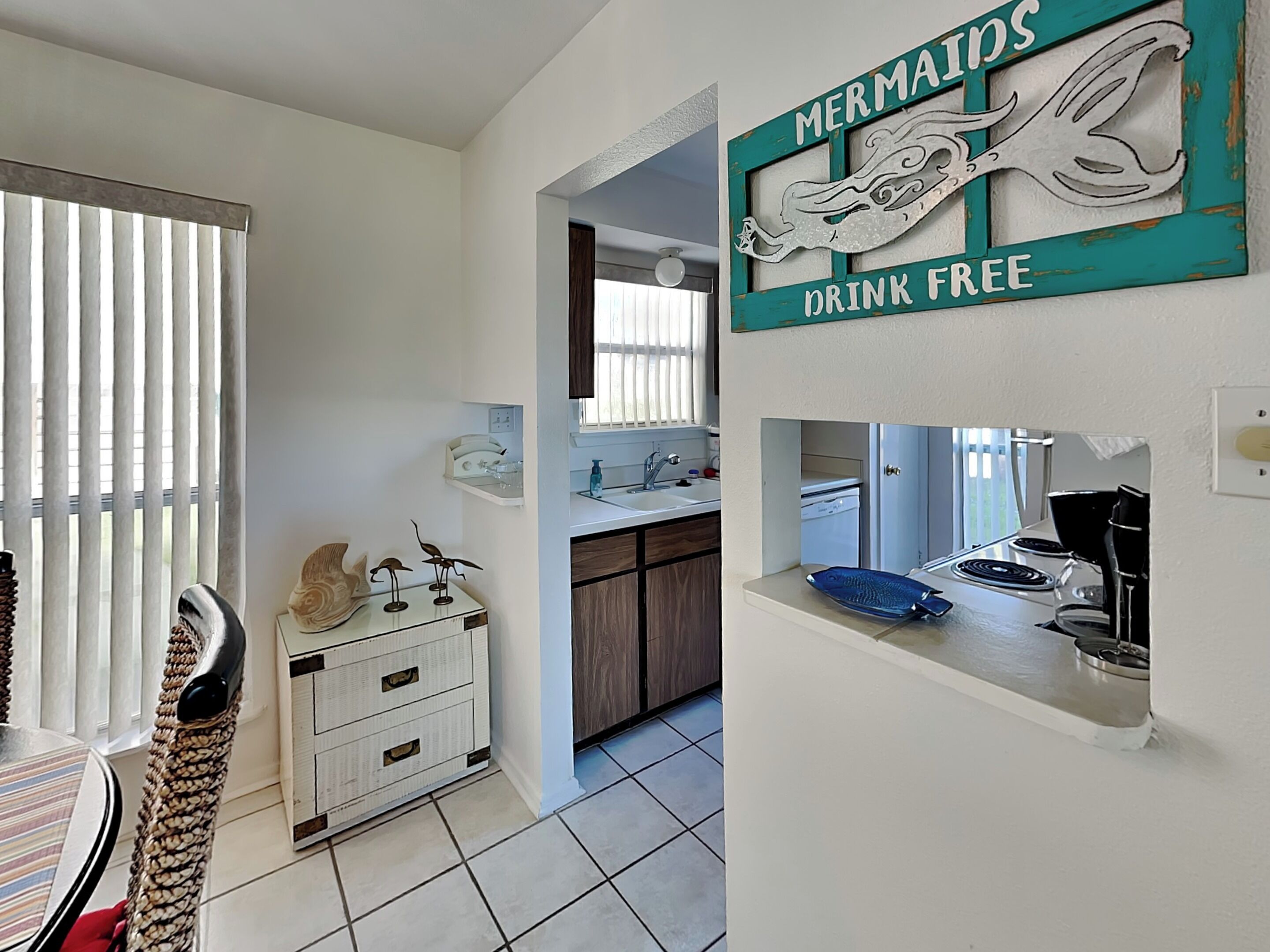 A kitchen with a sink, stove, and a decorative sign that reads "Mermaids Drink Free".