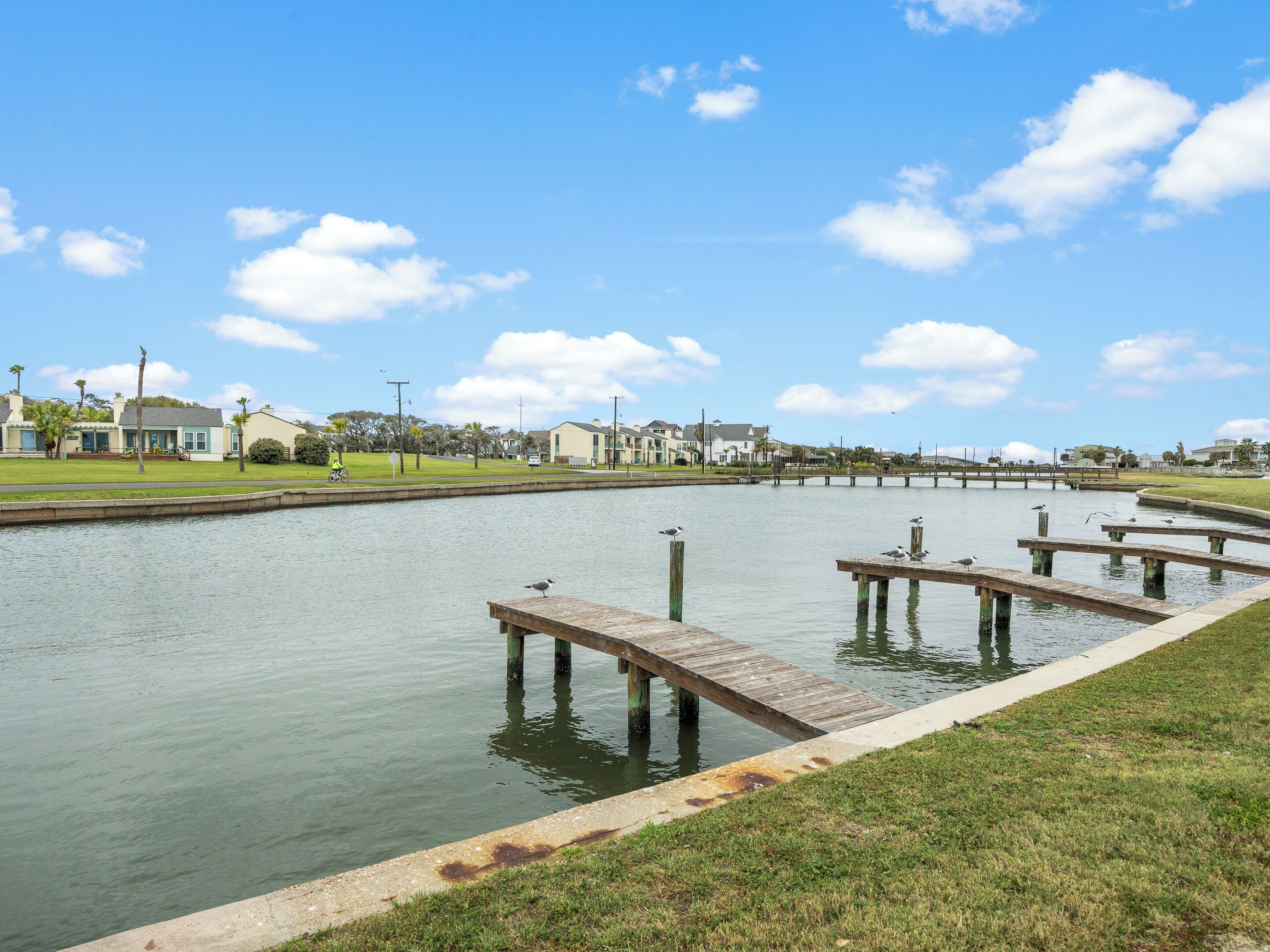 Una zona costera con un muelle, agua tranquila y edificios residenciales al fondo.