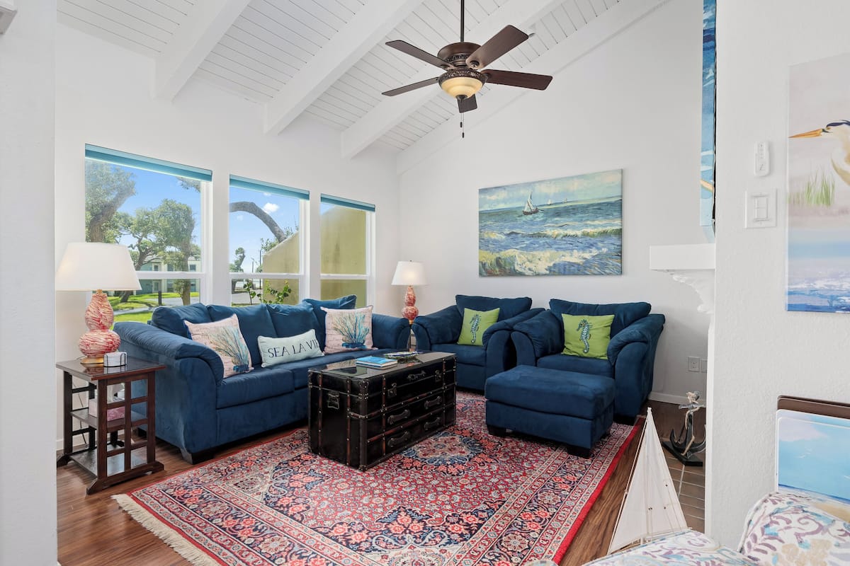 A living room with a blue sofa set, a patterned rug, and a ceiling fan.