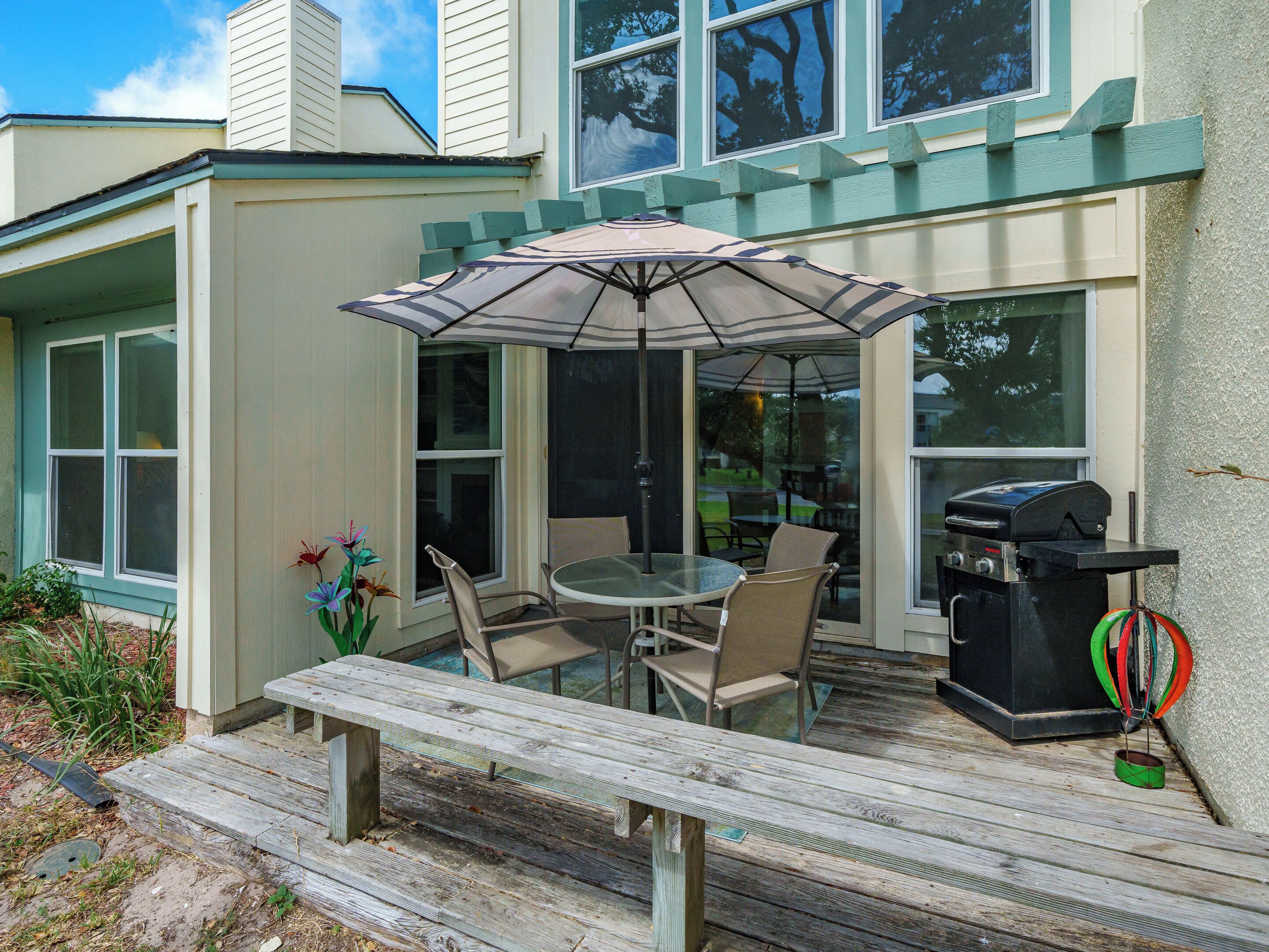 A patio with a table and chairs, a grill, and a wooden deck.