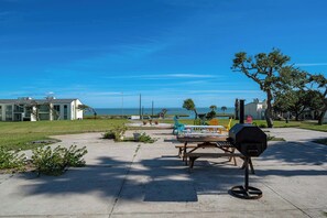 A patio area with picnic tables and a barbecue grill, overlooking a body of water and buildings. - Rockport Racquet and Yacht Club by Miss Kitty’s (Rockport)