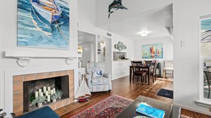 A spacious living room with a fireplace, a dining area with a table and chairs, and a kitchen visible in the background. - Rockport Racquet and Yacht Club by Miss Kitty’s (Rockport)