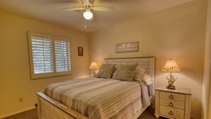 Un dormitorio con una cama de madera, dos mesitas de noche con lámparas, un ventilador de techo y una ventana con persianas.