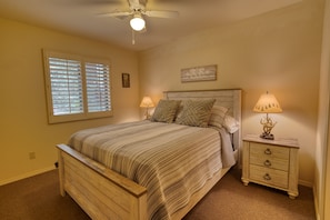 A bedroom with a wooden bed, two bedside tables with lamps, a ceiling fan, and a window with blinds.