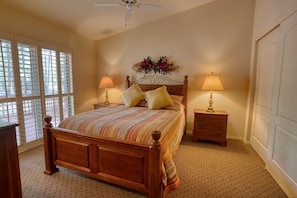 A bedroom with a wooden bed, two bedside tables with lamps, a decorative wall piece, and a window with blinds.