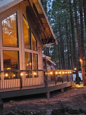 A cabin with large windows, a deck with railing, and a forested backdrop.