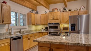 Una cocina con armarios de madera, encimeras de granito, electrodomésticos de acero inoxidable y una ventana con persianas.