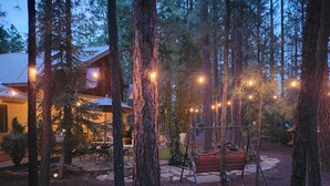 Un área boscosa al aire libre con una cabaña de madera, un conjunto de columpios y luces colgantes.