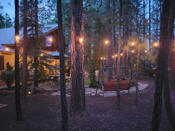 A forested outdoor area with a wooden cabin, a swing set, and string lights.