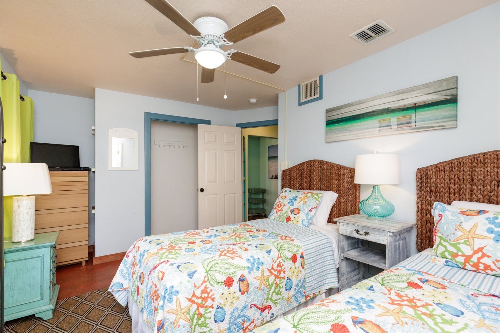 A bedroom with two beds, a ceiling fan, a TV on a dresser, and a painting on the wall.