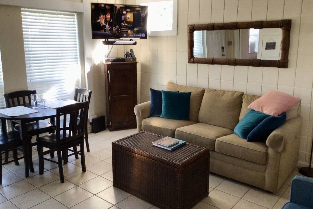 Una sala de estar con un sofá color beige, una mesita de centro, un televisor y un comedor con sillas y una mesa.