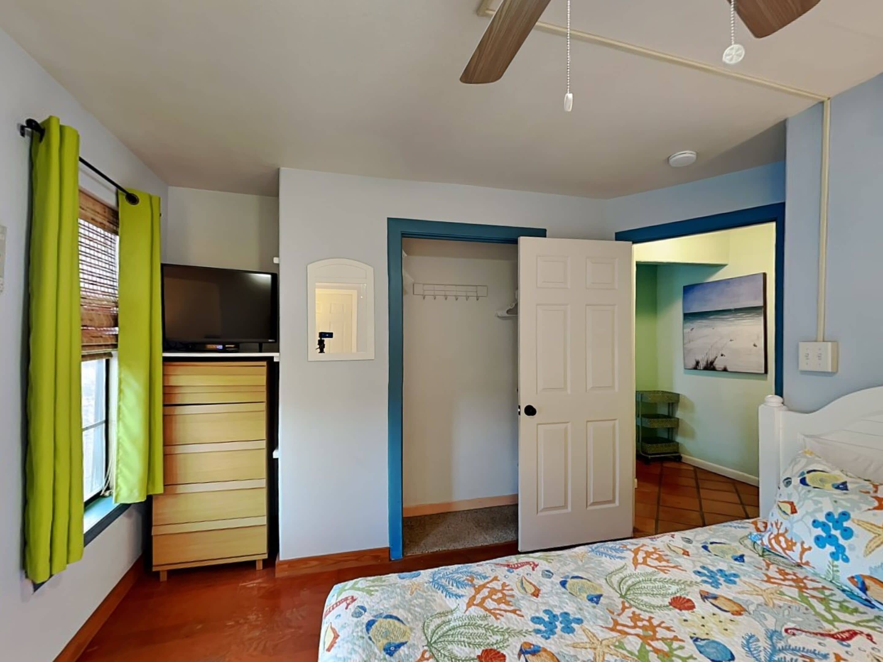 A bedroom with a bed, a desk, a television, a wardrobe, and a door leading to another room.