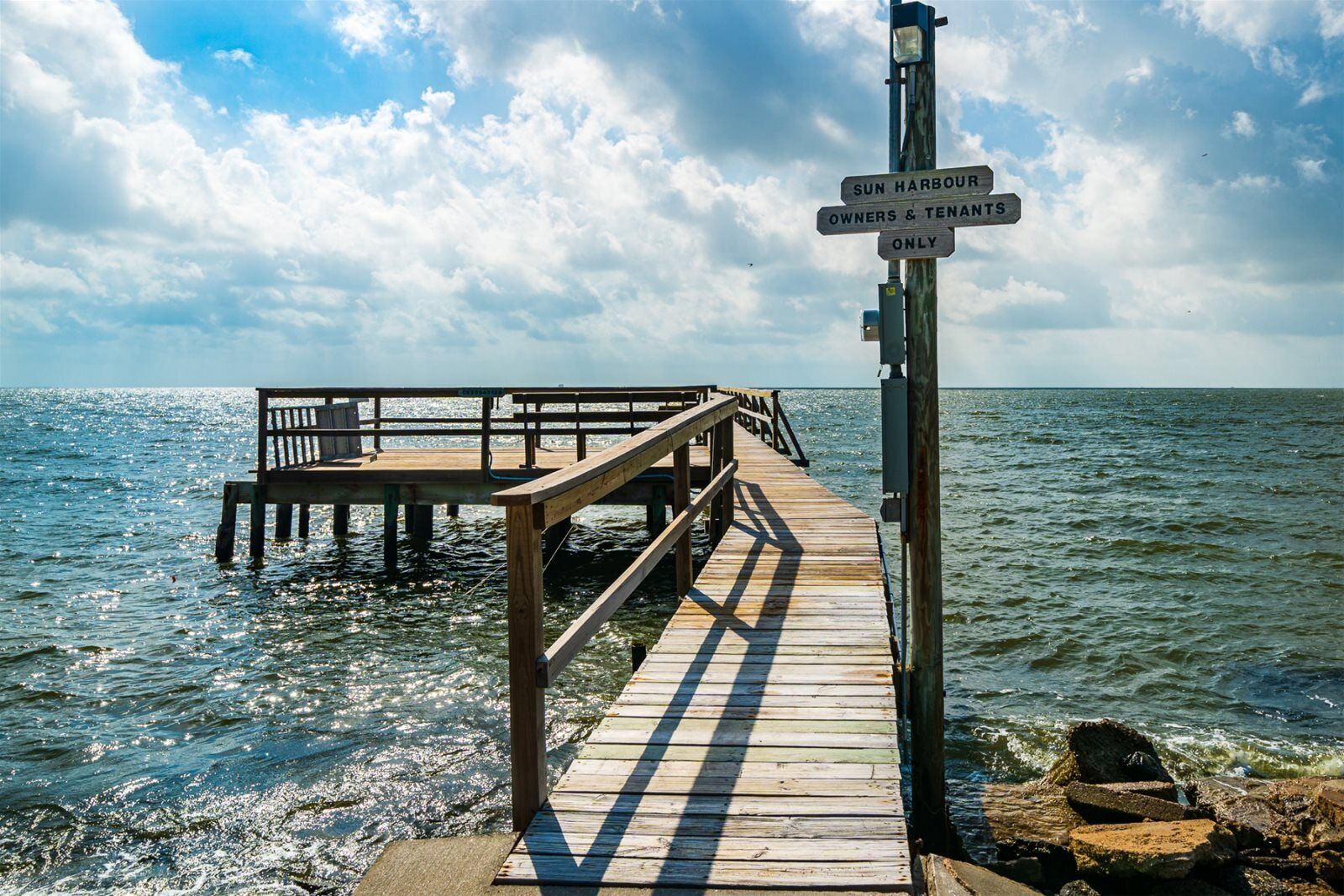 A wooden pier leading to a dock with a sign indicating 'SUN HARBOUR OWNERS & TENANTS ONLY'.