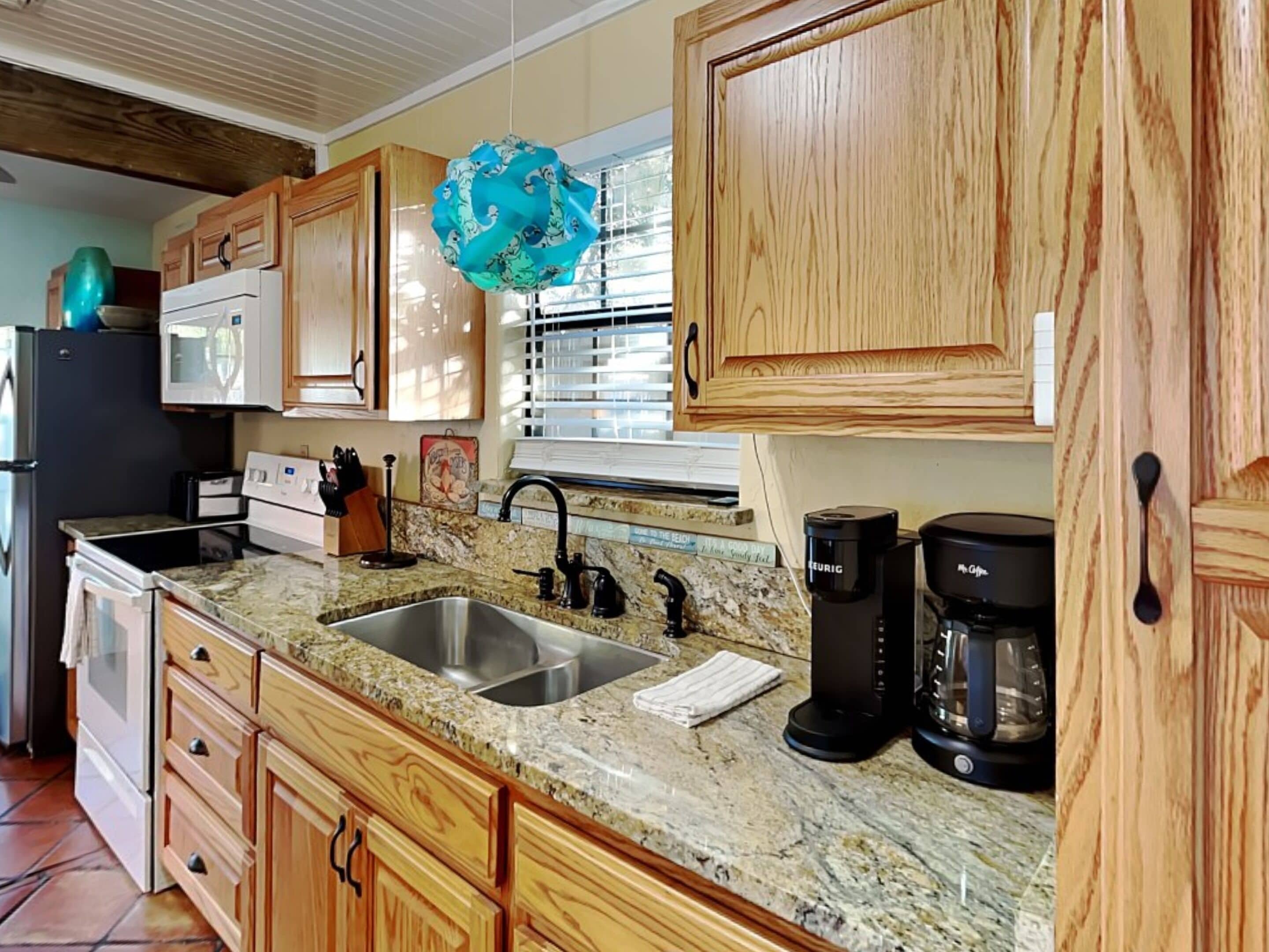 A kitchen with wooden cabinets, granite countertops, a stainless steel sink, a coffee maker, and a microwave.