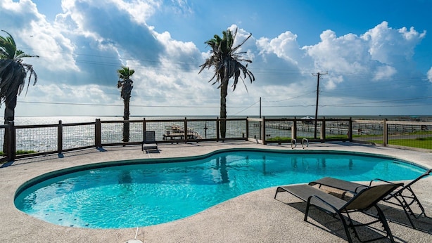 A swimming pool with lounge chairs, a wooden fence, and a view of the ocean. - Sun Harbor Cottages by Miss Kitty’s (Rockport)