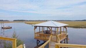 A wooden dock with a covered seating area extending into a calm body of water, surrounded by open fields and a clear sky. - Deep Water Dock and Home on the GA Coast (Midway)