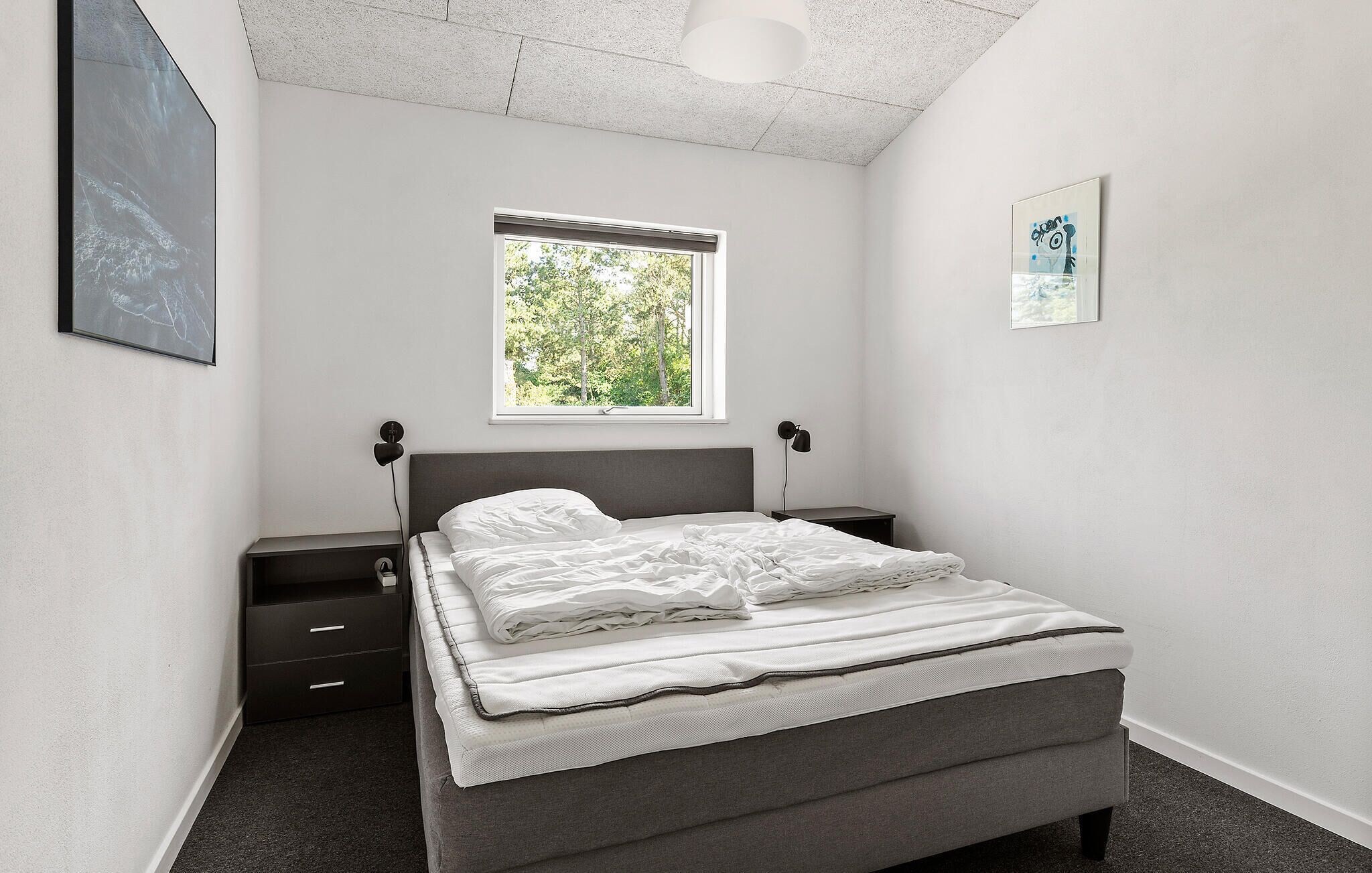 A bedroom with a bed, bedside tables, a window, and artwork on the walls.