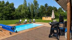 A wooden deck with a pool, lounge chairs, a barbecue grill, and a small shed.
