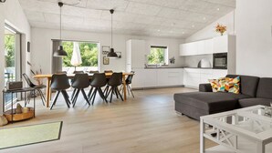 A modern kitchen with white cabinets, a dining area with a table and chairs, and a living area with a sofa and a coffee table.