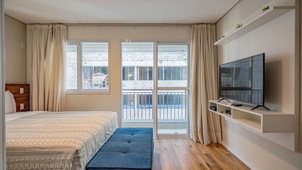 Ein Schlafzimmer mit Bett, einer Bank, einem Fernseher und einem Balkon mit Blick.