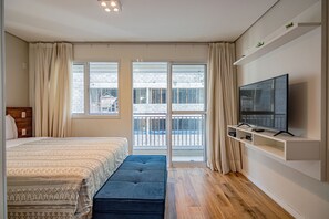Un dormitorio con cama, una banca, un televisor y un balcón con vistas.