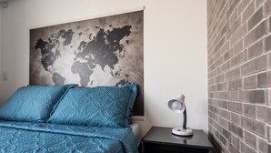 Ein Schlafzimmer mit Wandgemälde einer Weltkarte, einer blau gemusterten Bettdecke und einem Nachttisch mit Lampe.