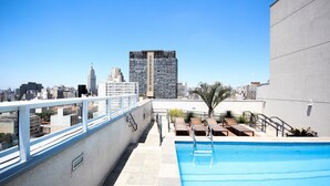 Ein Pool auf dem Dach mit Blick auf die Skyline der Stadt, eine Treppe, die zum Pool führt, und Sitzgelegenheiten im Freien.