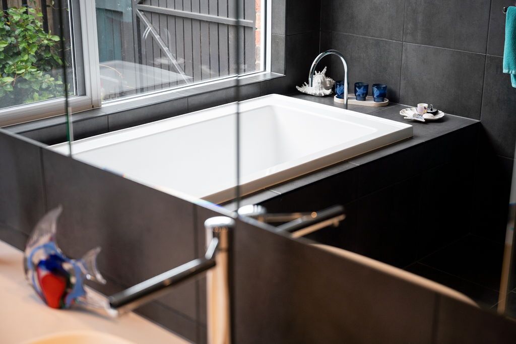 Une salle de bain moderne avec une grande baignoire rectangulaire, une douche en verre et des murs recouverts de carreaux foncés.