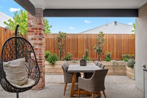 Un espace patio aménagé avec une table et des chaises, un fauteuil suspendu et une clôture en bois ornée de plantes.